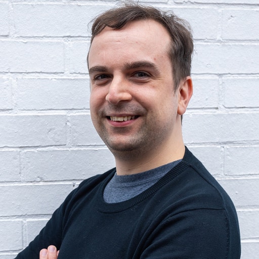 Ben Borthwick with his arms crossed in front of a white brick wall.