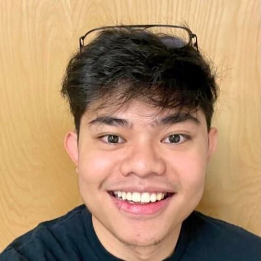 A young man smiling in front of a wooden wall, part of a Video Gamer Team.